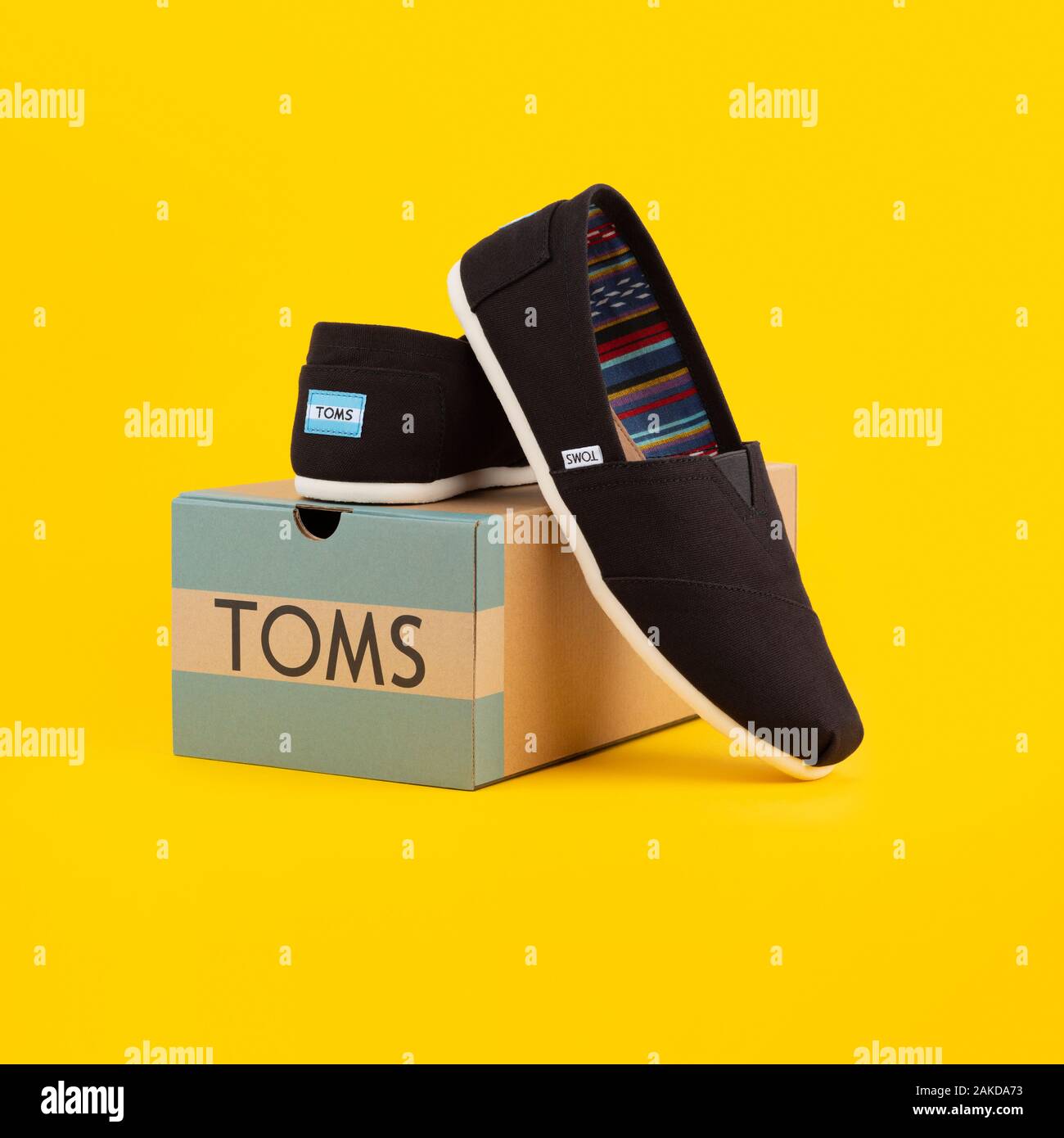 Una coppia di Toms Scarpe dalla società di raccolta di Venezia viene visualizzata da una scatola di scarpe di marca shot su sfondo giallo. Foto Stock