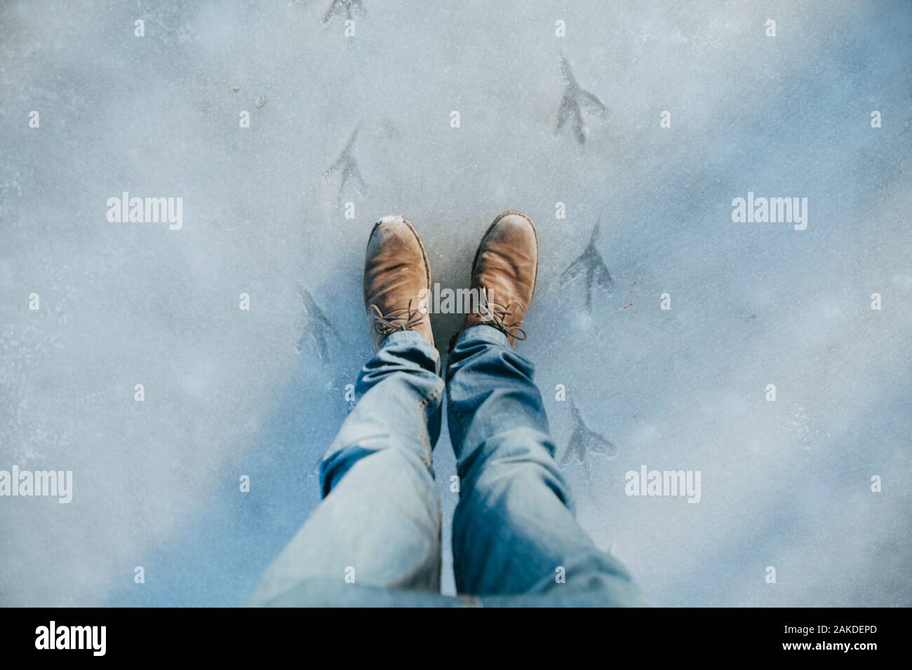 Primo piano delle gambe maschili nelle scarpe invernali in piedi sul lago di ghiaccio Foto Stock