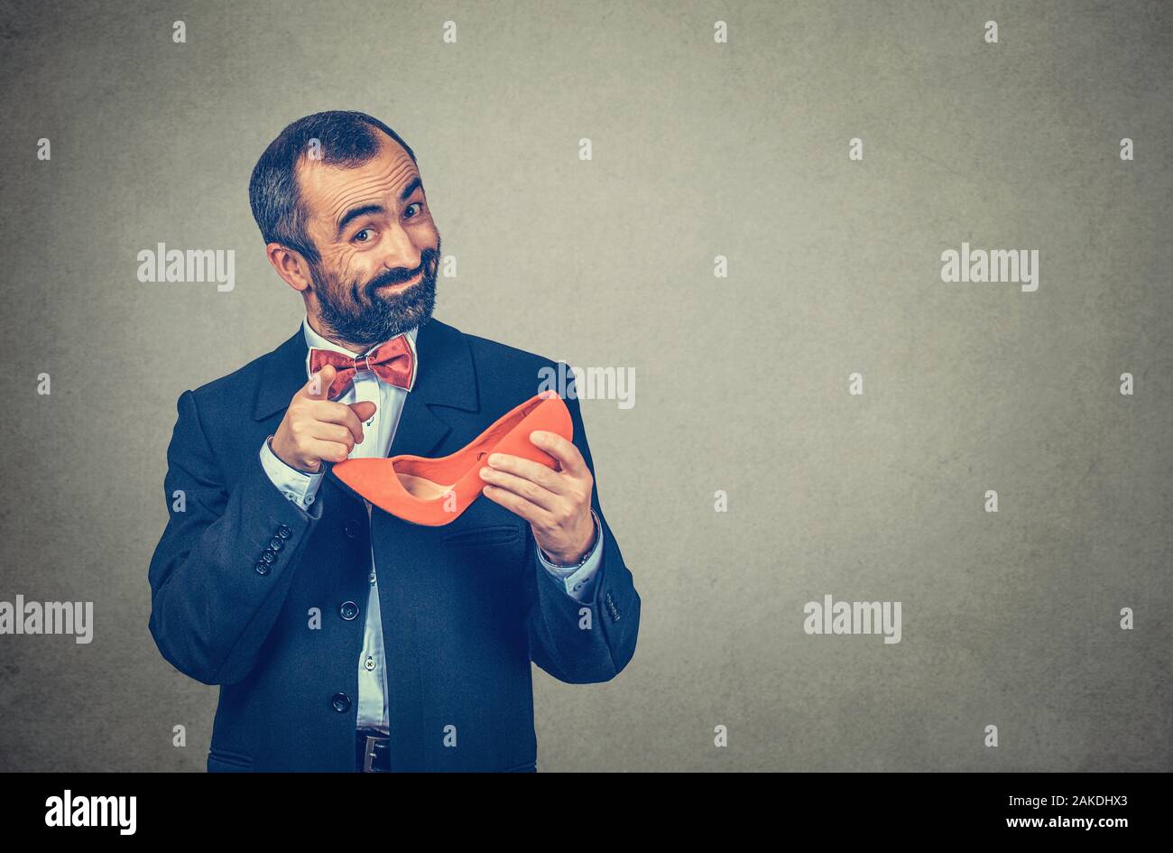 Si consiglia di indossare tacchi. Imprenditore barbuto, uomo tenendo un rosso ad alta-scarpe con tacco, puntando con il dito alla telecamera chiedendo quale è la vostra. A mezza lunghezza corpo. Foto Stock