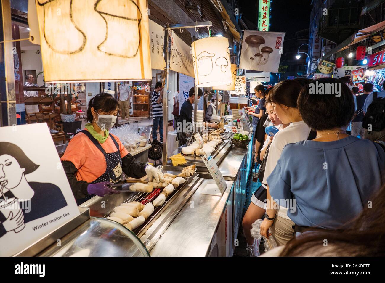 Una donna grigliava funghi di ostriche per una coda di clienti in una stalla di cibo nel mercato notturno di Shi Lin, Taipei, Taiwan Foto Stock