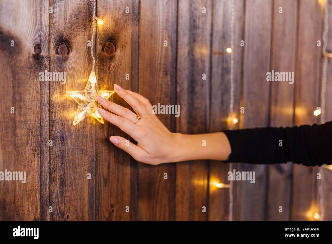 Donna di mano toccando natale decorazione luminosa stella sulla parete in legno. Vacanze di Natale concept Foto Stock