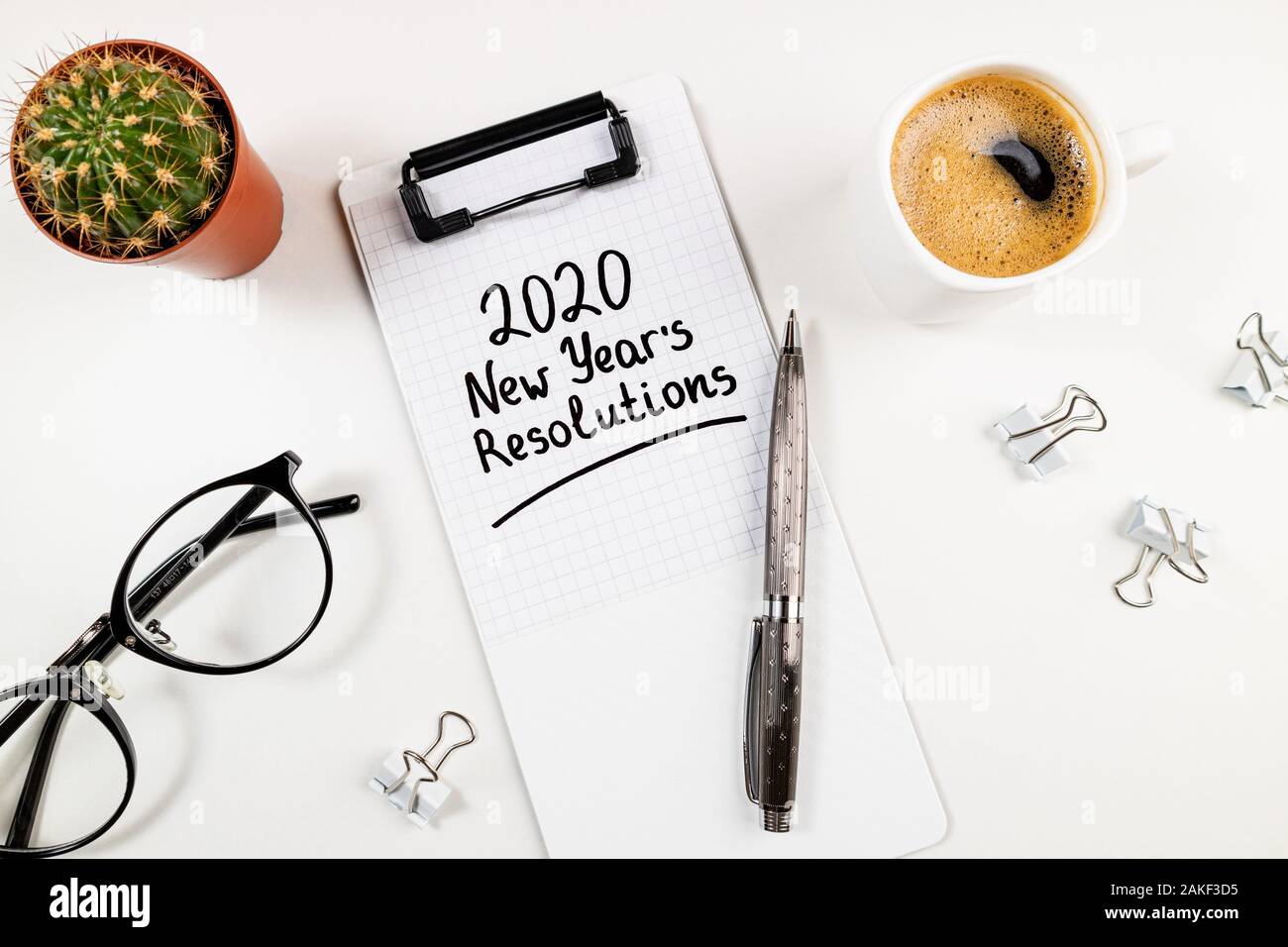 Propositi per l'anno nuovo 2020 sulla scrivania. 2020 Elenco degli obiettivi con i notebook, tazza di caffè e bicchieri su sfondo bianco. Obiettivi, piano, strategia, risoluzioni, chan Foto Stock