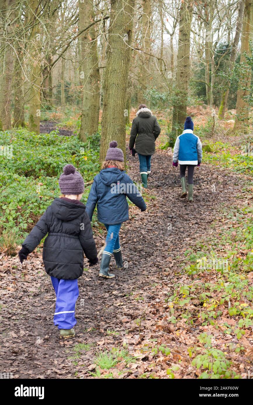 Madre / mamma / mamma camminando attraverso il fango con i suoi tre bambini in una giornata invernale su un percorso fangoso attraverso boschi sul West End Common, Esher, Surrey. REGNO UNITO. (115) Foto Stock