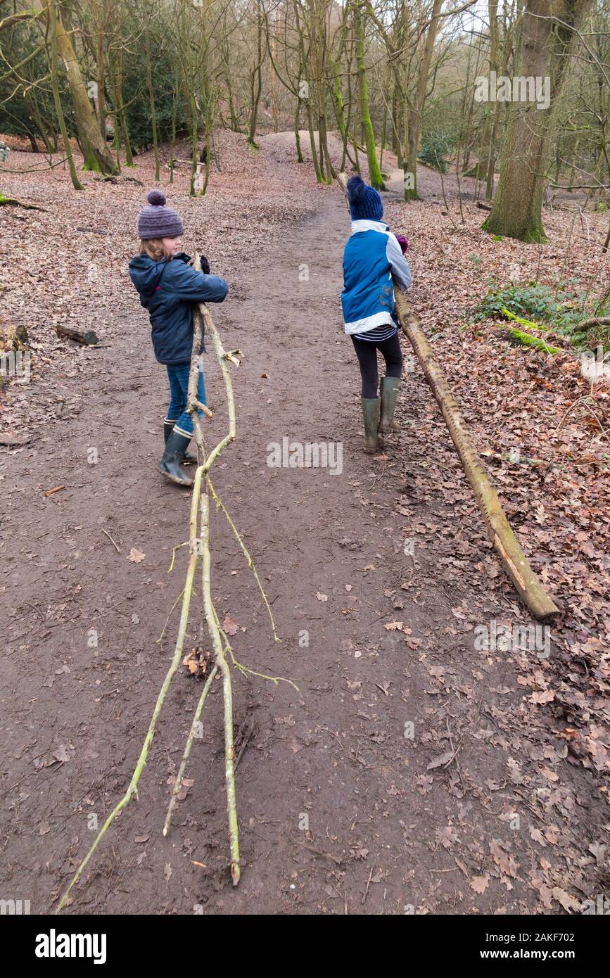Bambini / bambini / bambini / ragazze che trasportano raccolta alberi rami come parte della Forest School - una giornata invernale in boschi nel West End Common, Esher, Surrey. INGHILTERRA (115) Foto Stock