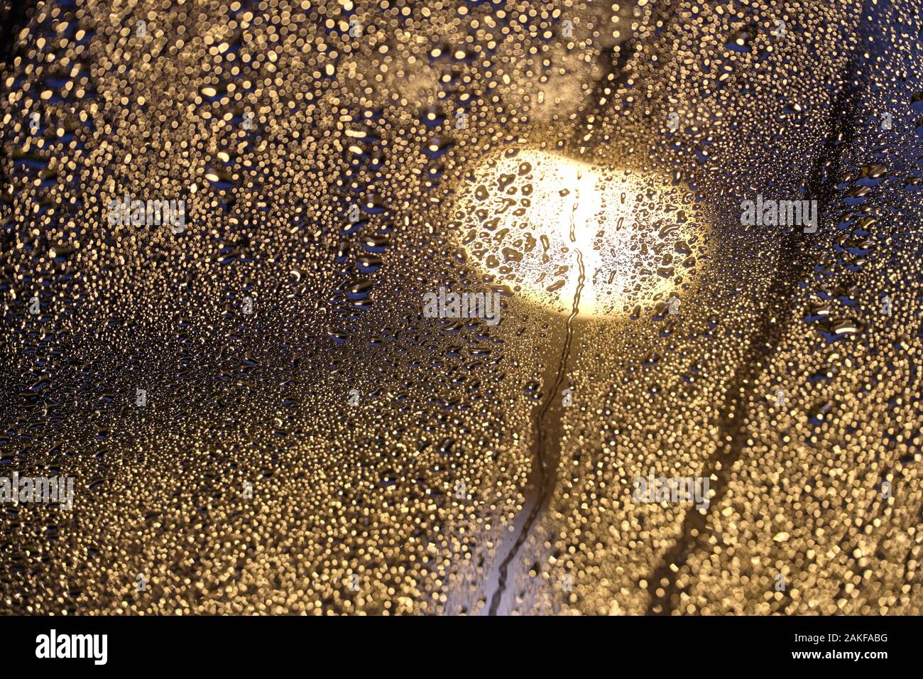 Moody foto luminose di scintillanti gocce di pioggia sul vetro nella parte anteriore di un lampione di notte. Visto in un giorno di pioggia in Germania nel mese di gennaio su una finestra a tetto Foto Stock