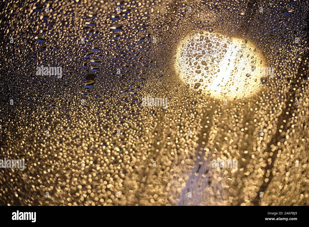 Moody foto luminose di scintillanti gocce di pioggia sul vetro nella parte anteriore di un lampione di notte. Visto in un giorno di pioggia in Germania nel mese di gennaio su una finestra a tetto Foto Stock