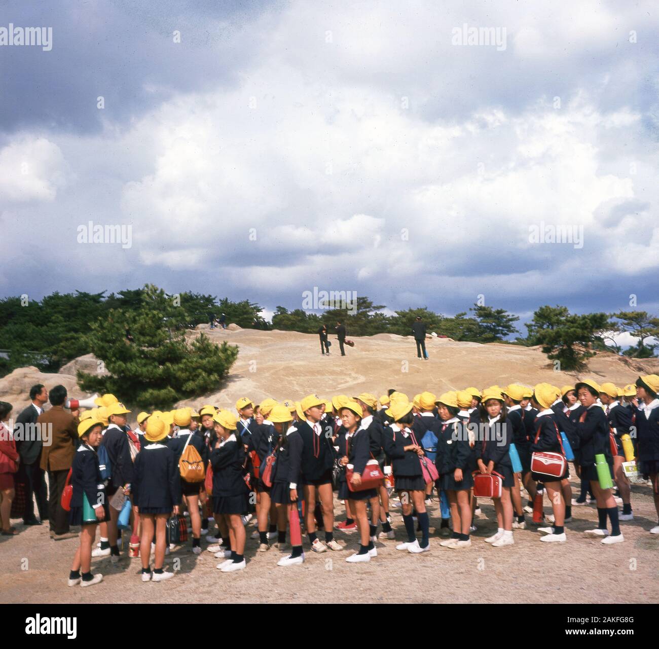Anni sessanta, storico gruppo di scuola giapponese i bambini in gita scolastica tutti vestiti in uniformi di blu e giallo cappello da sole. Foto Stock