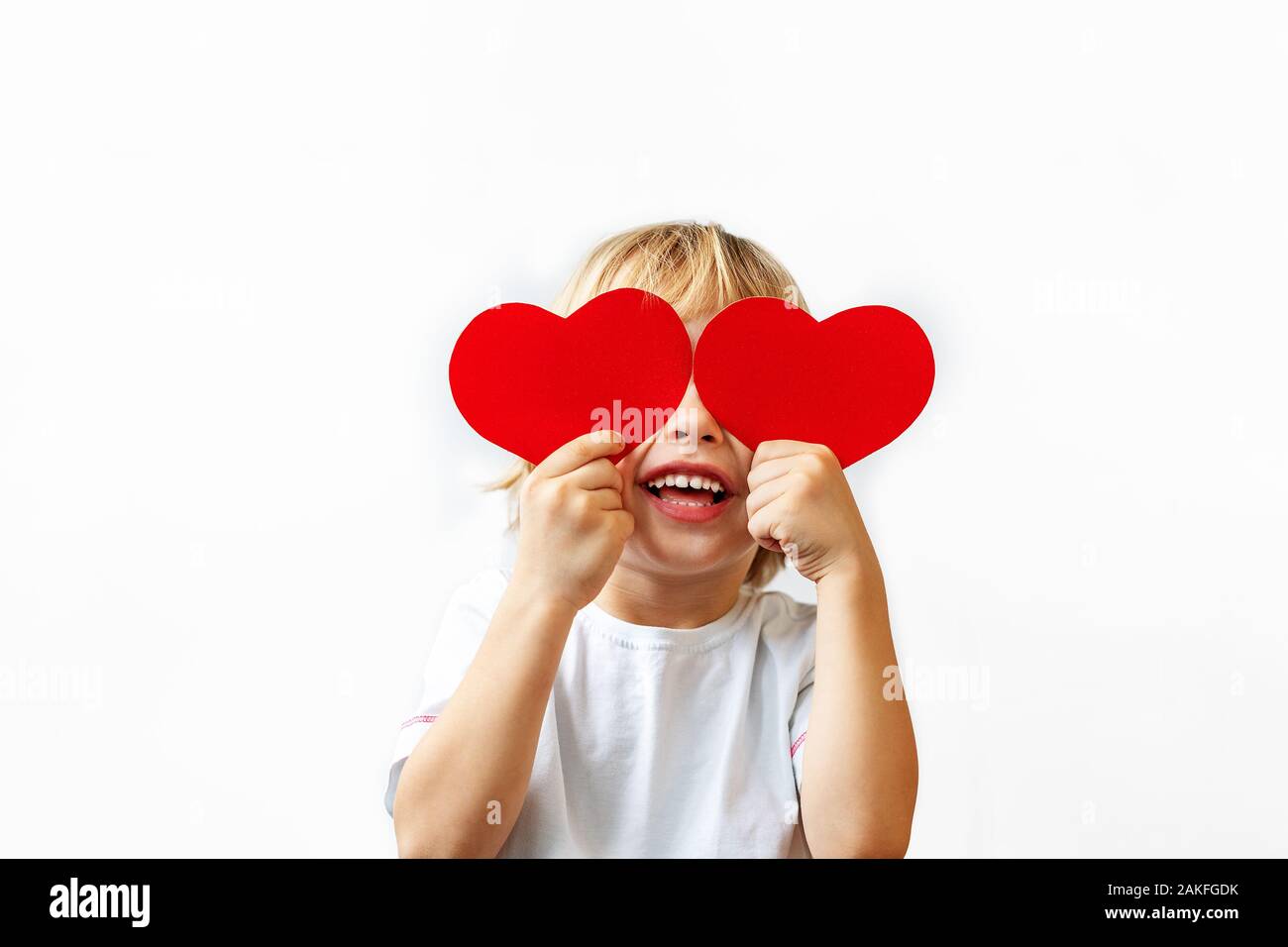 Un ragazzino in una camicia bianca contiene cuori rossi nelle sue mani,  chiude gli occhi e sorrisi su uno sfondo bianco. Il giorno di San  Valentino, Festa della Mamma, International Womens day