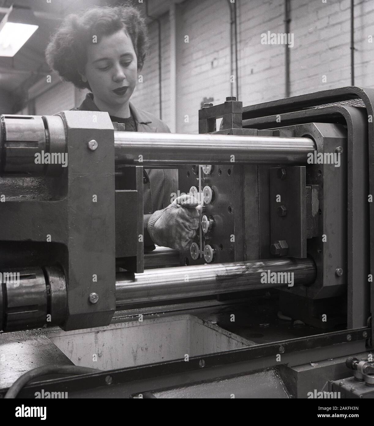 Degli anni Cinquanta, storico, femmina operativa di fabbrica funzionante a macchinario industriale in una batteria di fabbrica di fabbricazione, Inghilterra, Regno Unito. Foto Stock