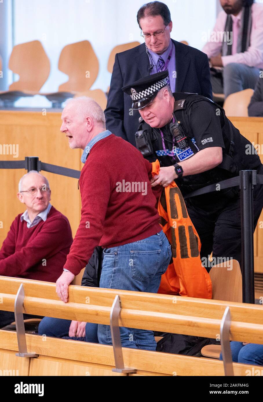 Un cambiamento climatico protester viene rimosso dalla polizia di galleria del pubblico durante il primo ministro di domande presso il parlamento scozzese di Edimburgo. Foto Stock