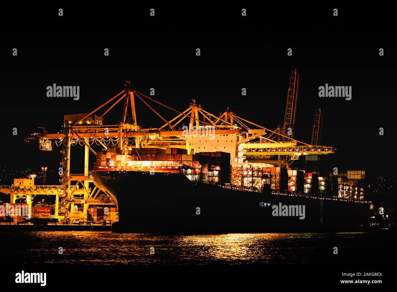 Vista notturna del porto di Trieste dal mare mediterraneo. lo sbarco di una nave portacontainer con gru giallo Foto Stock