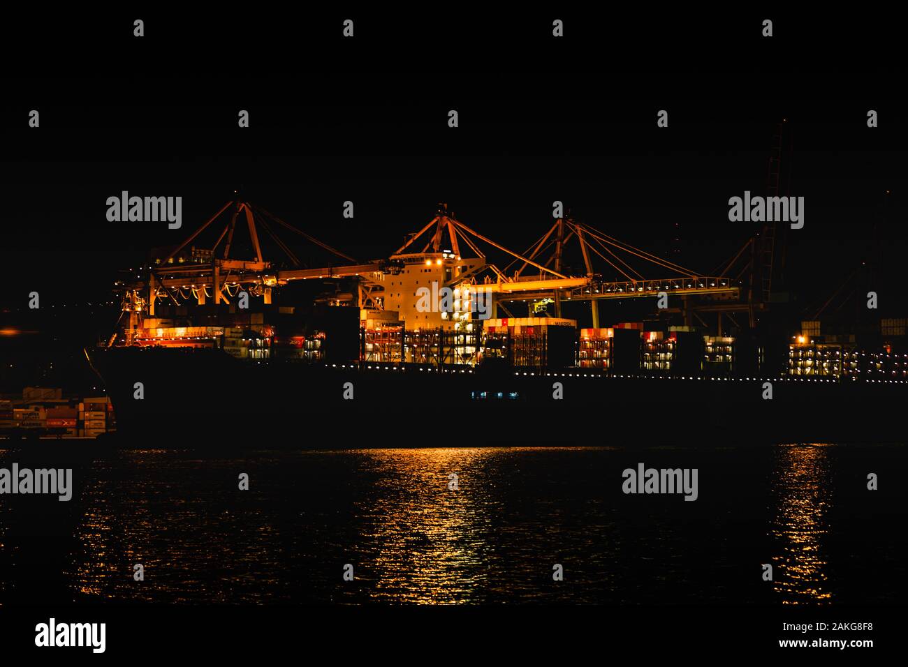 Vista notturna del porto di Trieste dal mare mediterraneo. lo sbarco di una nave portacontainer con gru giallo Foto Stock