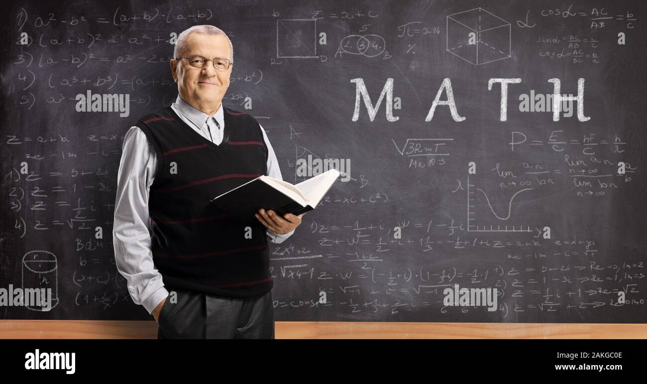 Maschio anziano maestro in possesso di un libro di fronte a una lavagna di matematica Foto Stock