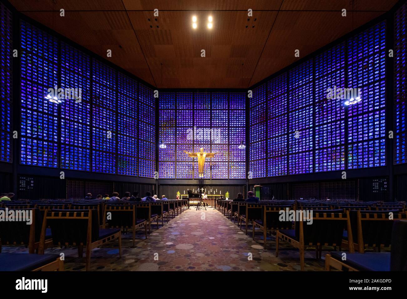 Vista simmetrica dell'interno della chiesa commemorativa Kaiser Wilhelm, con blocchi di vetro blu e viola e un crocifisso dorato alla fine della navata Foto Stock