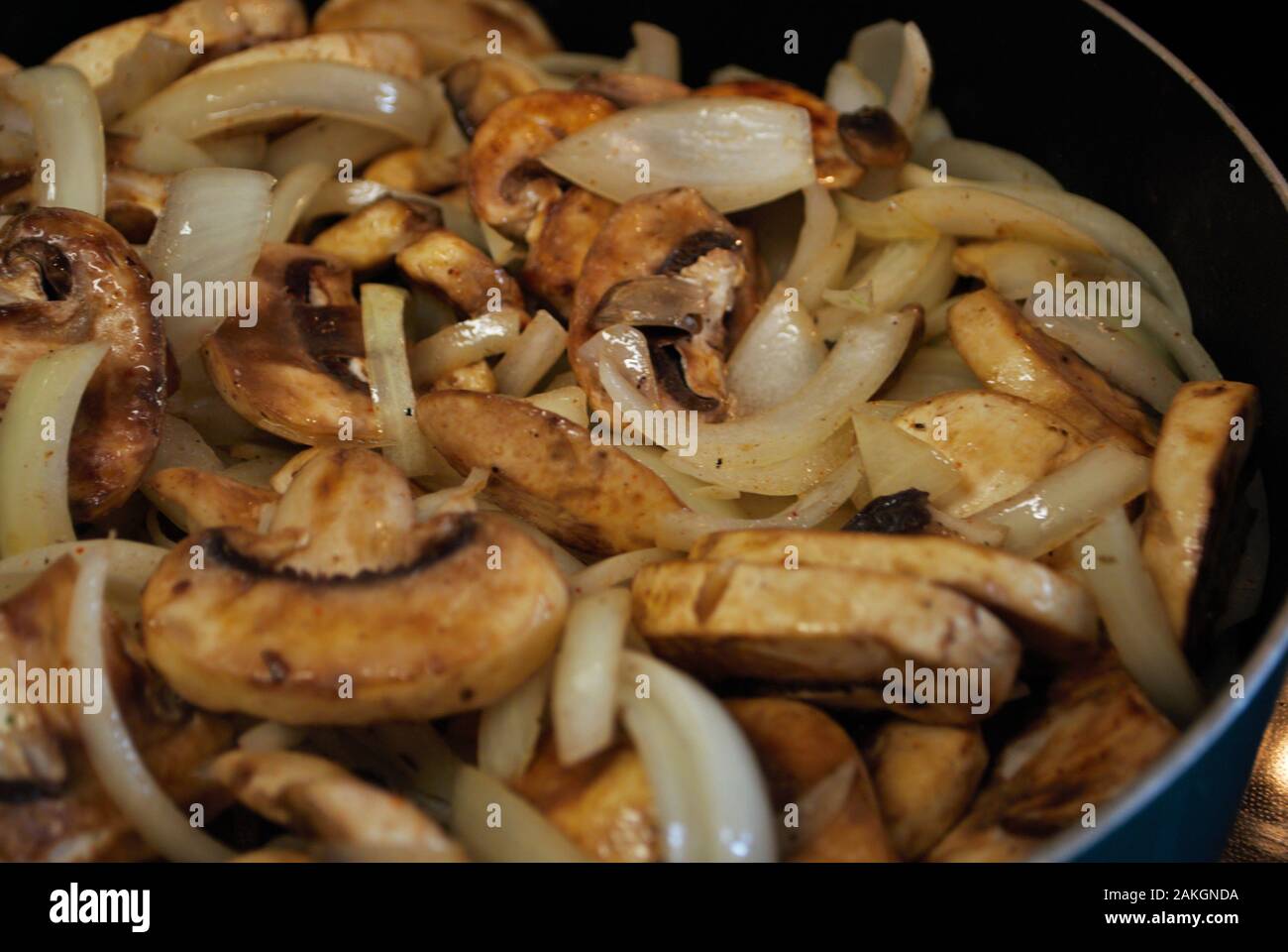 Sauteing i funghi e le cipolle in una padella con olio, condimento, e vapore Foto Stock