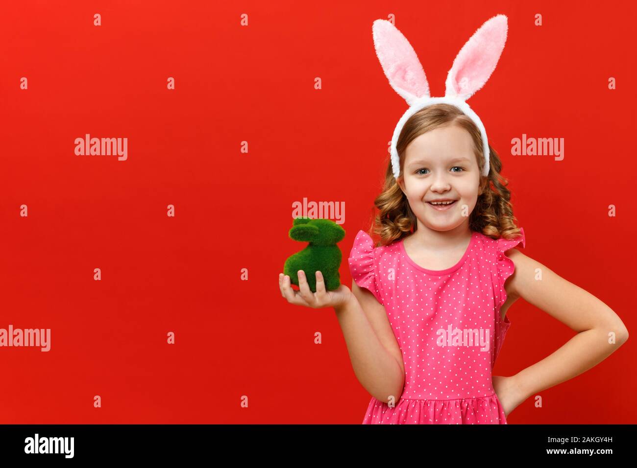 Felice Pasqua. Carino bambina nelle orecchie di coniglietto detiene un coniglio verde. Closeup bambino su un rosso sfondo colorato. Foto Stock