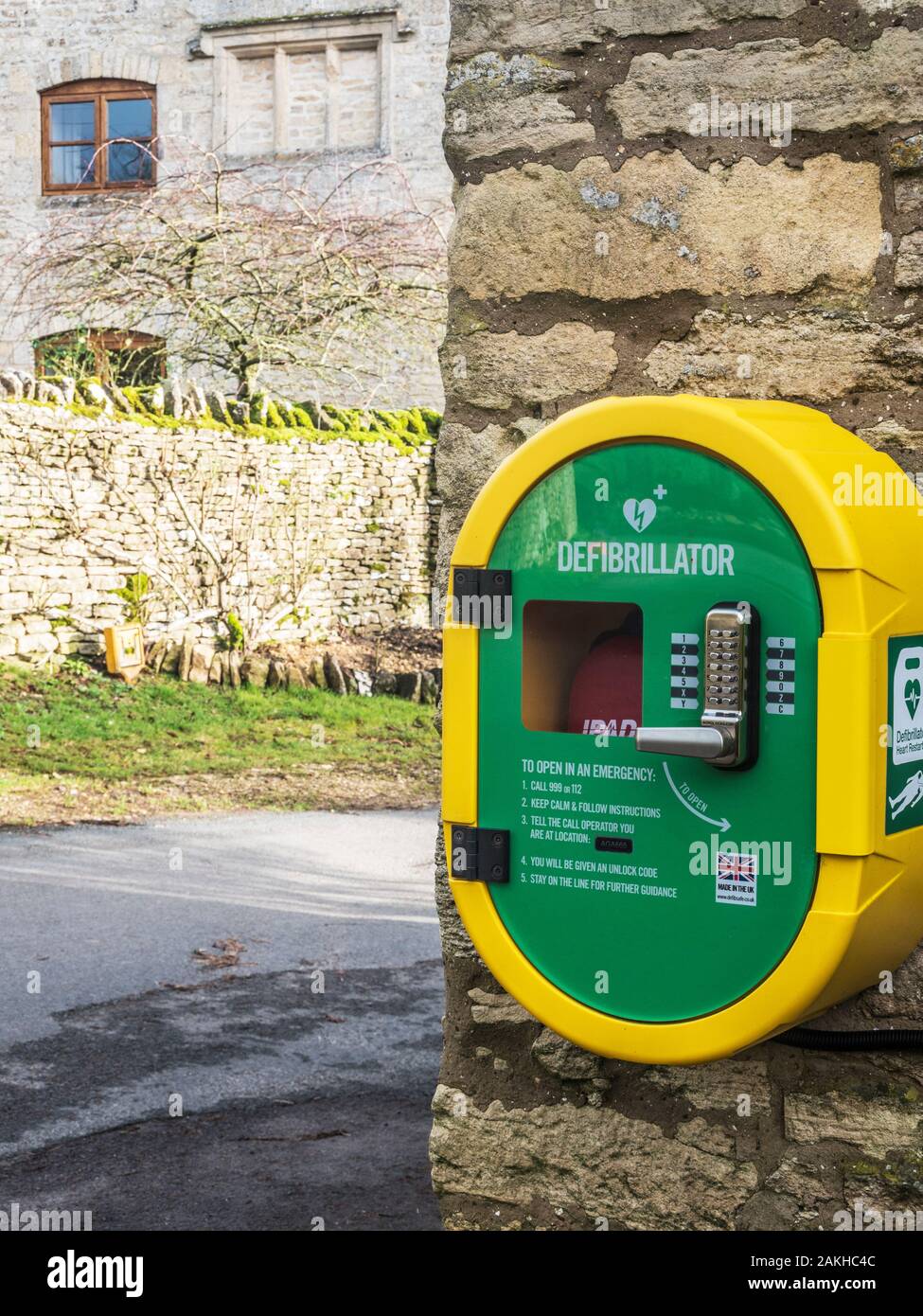 Un moderno pubblico accesso defibrillatore fissato ad una parete di pietra dal lato della strada di un paese. Foto Stock