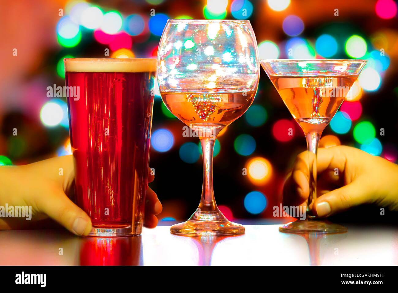 Una chiusura di un paio di persone la mano con una birra, un bicchiere di vino e un martini e luci colorate sullo sfondo Foto Stock