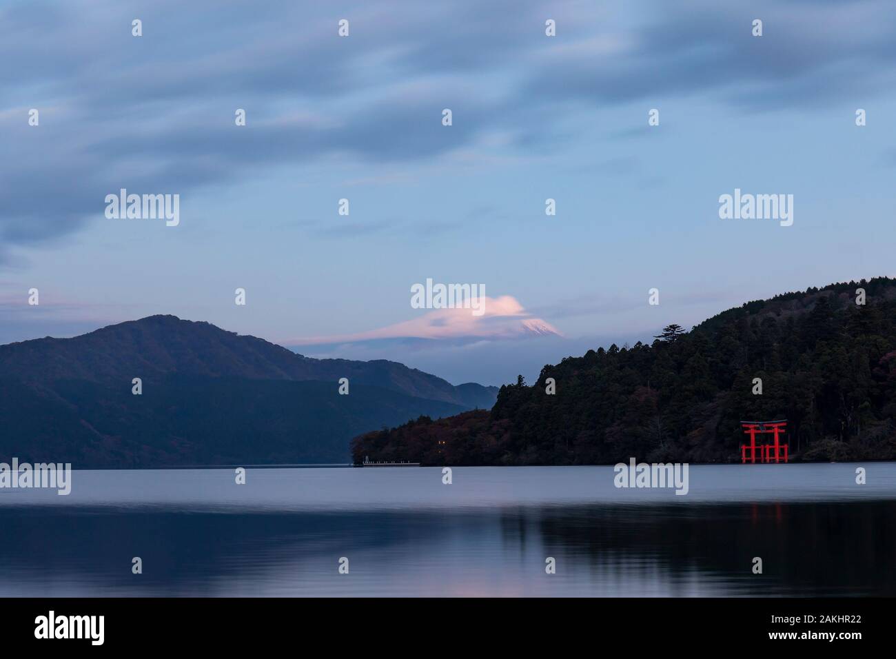Un torii gate sulla banca del lago Motohakone all'alba. Il monte Fuji può essere visto in background e il suo vertice dalle nubi. Foto Stock