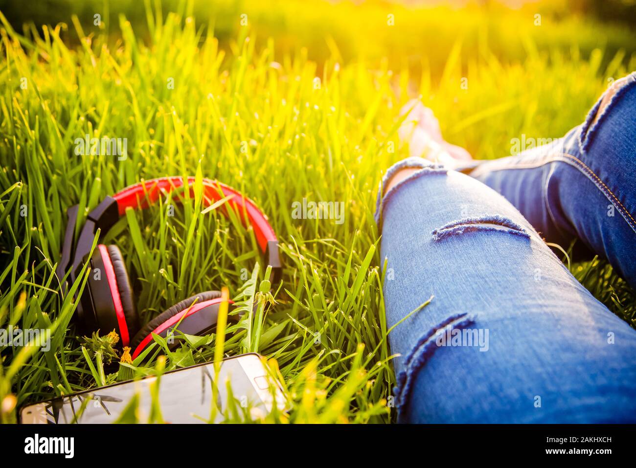 Gambe di hipster donna che indossa jeans strappati giacente in erba verde  lo smartphone con auricolari e godersi il tramonto - estate relax Foto  stock - Alamy