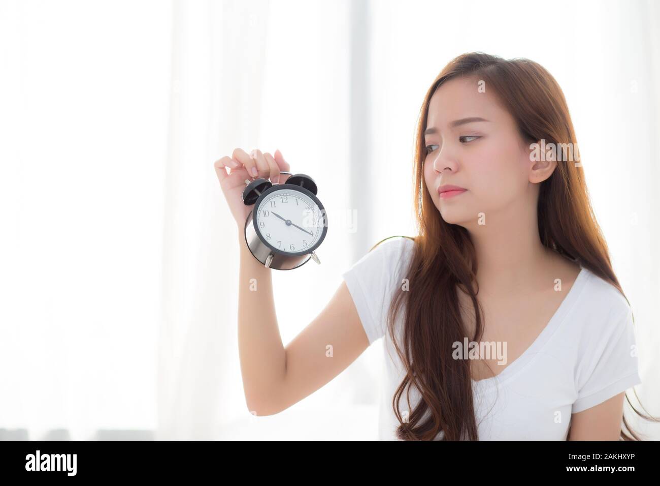 Bella giovane donna asiatica svegliarsi al mattino infastiditi sveglia tenendo la mano, ragazza in piedi fretta wake tardi con appuntamento con tendina backgroun Foto Stock