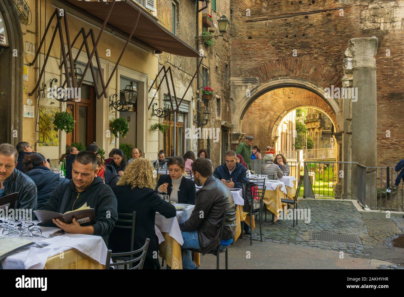 La gente sta mangiando all'aperto in una trattoria tipica in Ghetto, quartiere ebraico di Roma, con Portico di Octavia (Portico di Ottavia) sullo sfondo Foto Stock
