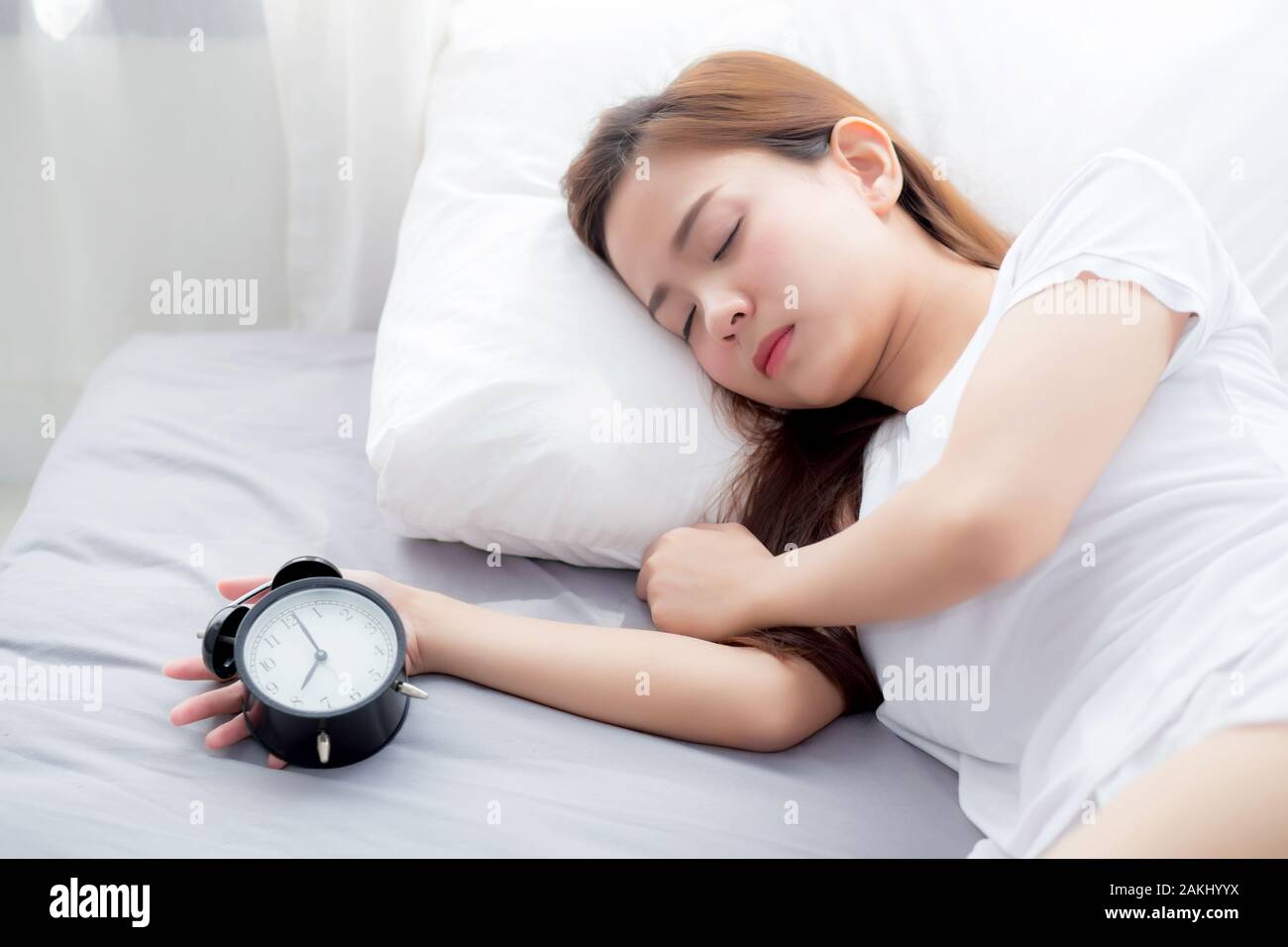 Bella asiatica giovane donna disattivare la sveglia di buon mattino per dormire, ragazza con sveglia, tempo e concetto di stile di vita. Foto Stock