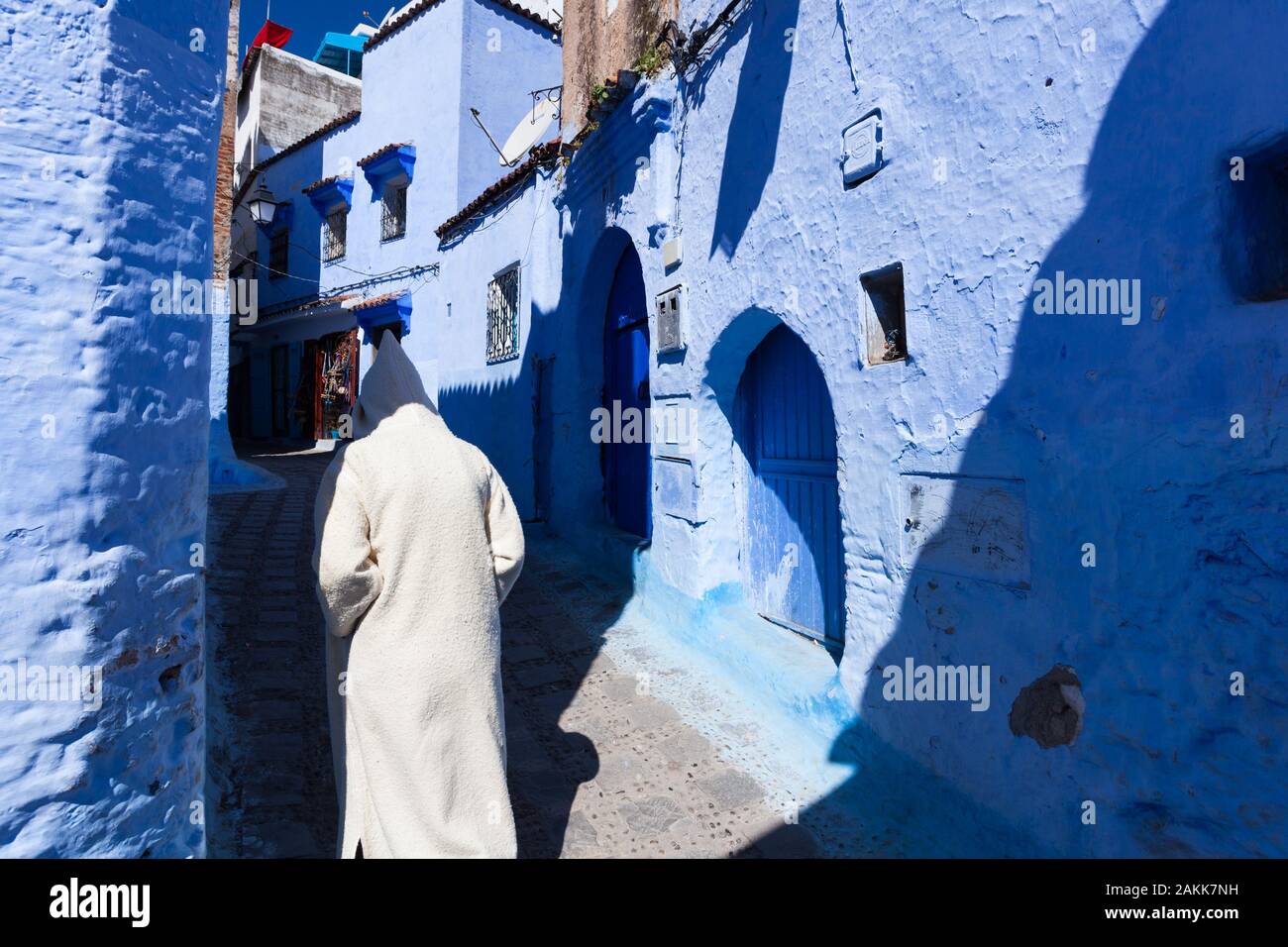 Un uomo solitario indossando djellaba luminoso con cappuccio che copre la sua testa a piedi in strada della medina di Chefchaouen (noto anche come Chaouen), Marocco Foto Stock