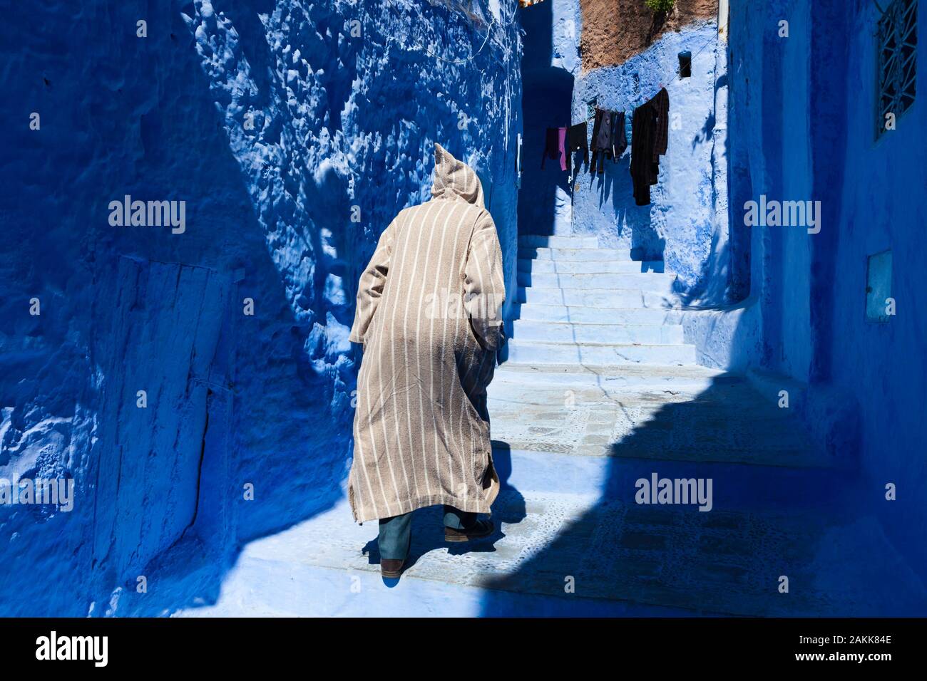 Uomo in djellaba a strisce che cammina fino le scale nella stretta strada della medina a Chefchaouen (conosciuto anche come Chaouen), Marocco Foto Stock
