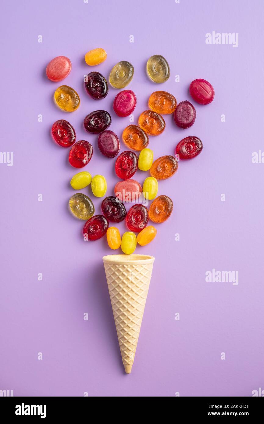 Dolci caramelle colorate in cono gelato su sfondo viola. Vista piana. Foto Stock