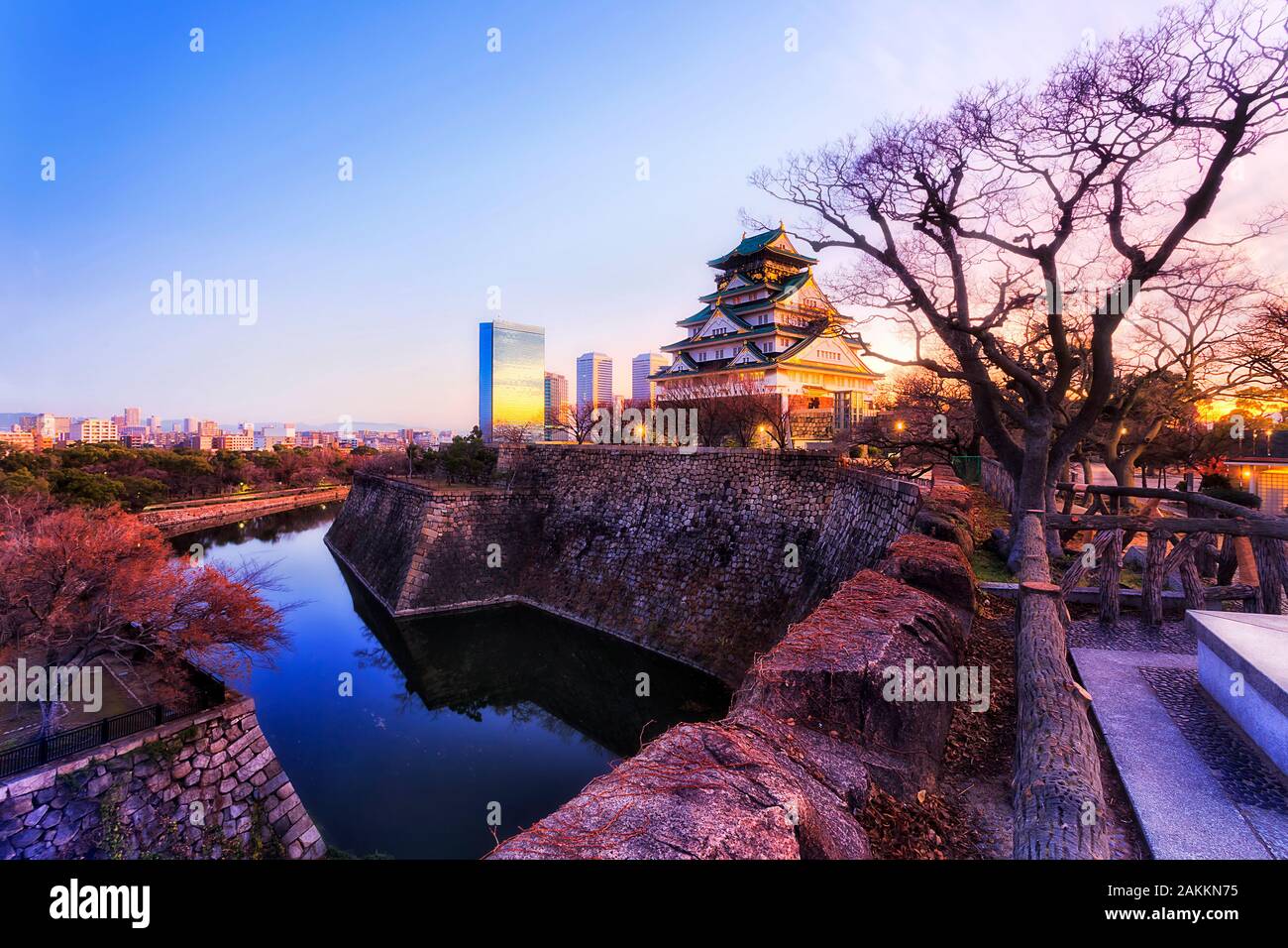 Il mantenere principale del castello di Osaka da shogun volte aumento oltre i muri di pietra e acqua riempito fossati presso sunrise contro il cielo chiaro e moderno distanti busines Foto Stock