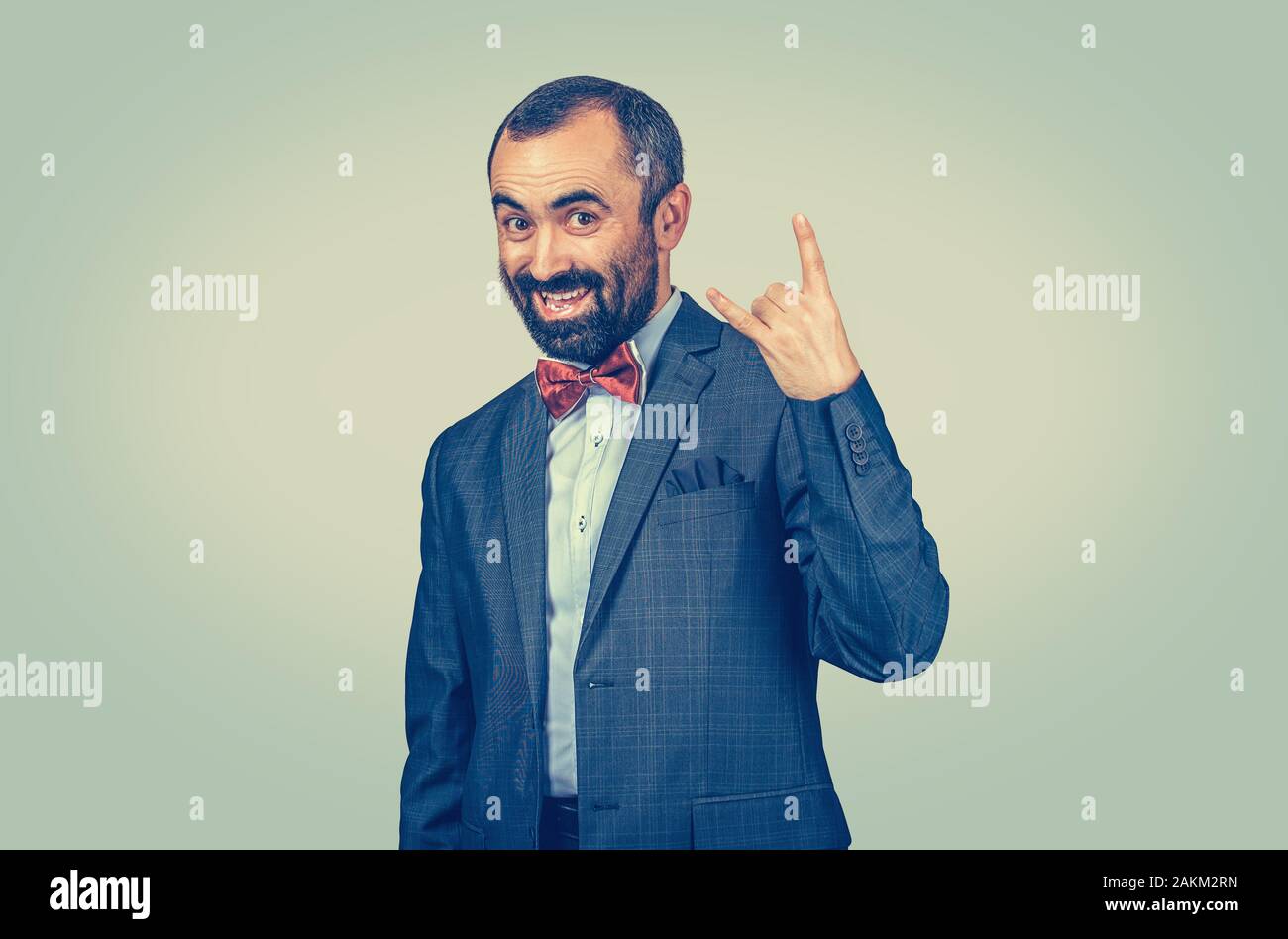 Funny barbuto imprenditore mostra di metallo pesante gesto mano paglierino su sfondo verde. Espressione facciale sensazione simbolo, il linguaggio del corpo, non verbale com Foto Stock