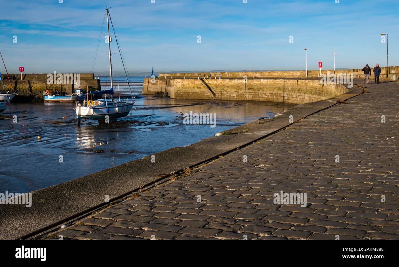 Barche a vela a terra nel fango con bassa marea con lunghe mura ricurve del porto, Fisherrow Harbour, Musselburgh, Scozia, Regno Unito Foto Stock