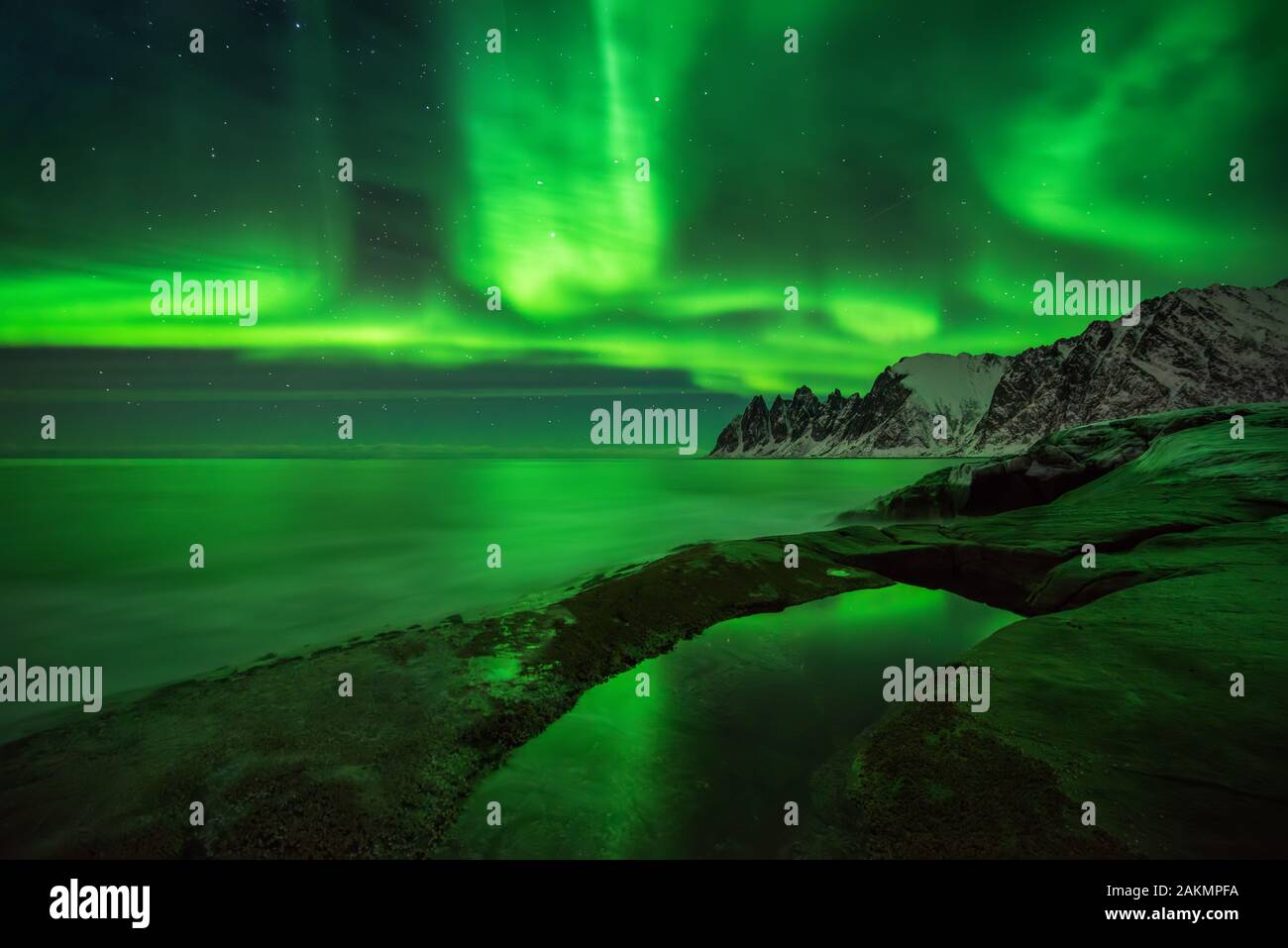 Aurora su Tugeneset costa rocciosa con Okshornan montagne sullo sfondo, Senja, Norvegia Foto Stock