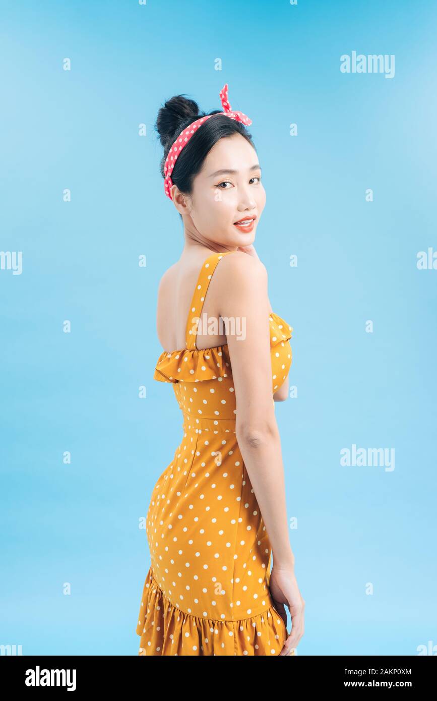 Grazioso alla moda giovane donna in posa su sfondo blu. Romantico adorabile ragazza di polka dot abito giallo Foto Stock