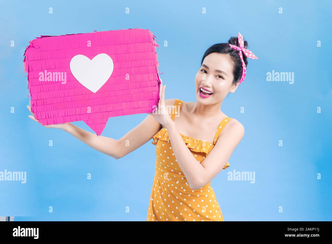 Ritratto di una allegra donna africana in piedi isolato su sfondo blu che mostra discorso bolla con icona a forma di cuore Foto Stock