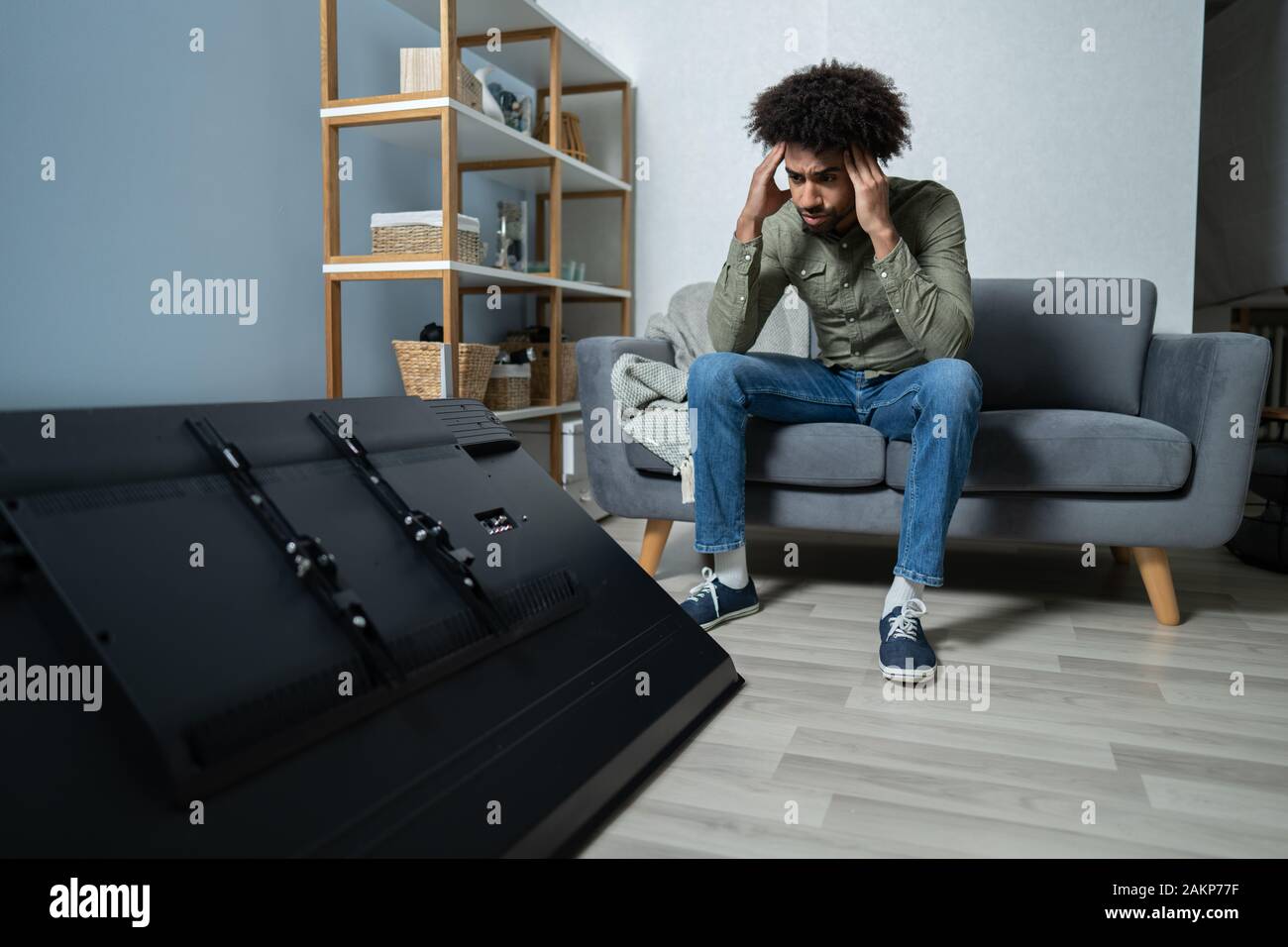 Uomo seduto sul divano davanti caduti televisione con schermo rotto Foto Stock