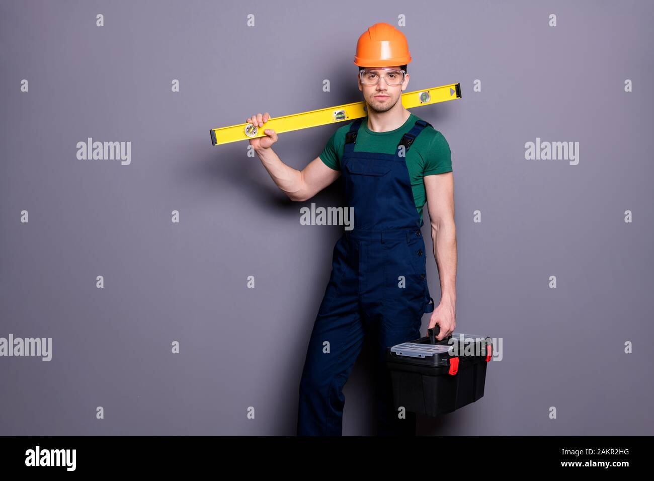 Foto di bel mascolino tecnico esperto tenere misura rack cassetta utensile pronto per iniziare a lavorare indossare t-shirt sicurezza Dungarees casco protettivo Foto Stock
