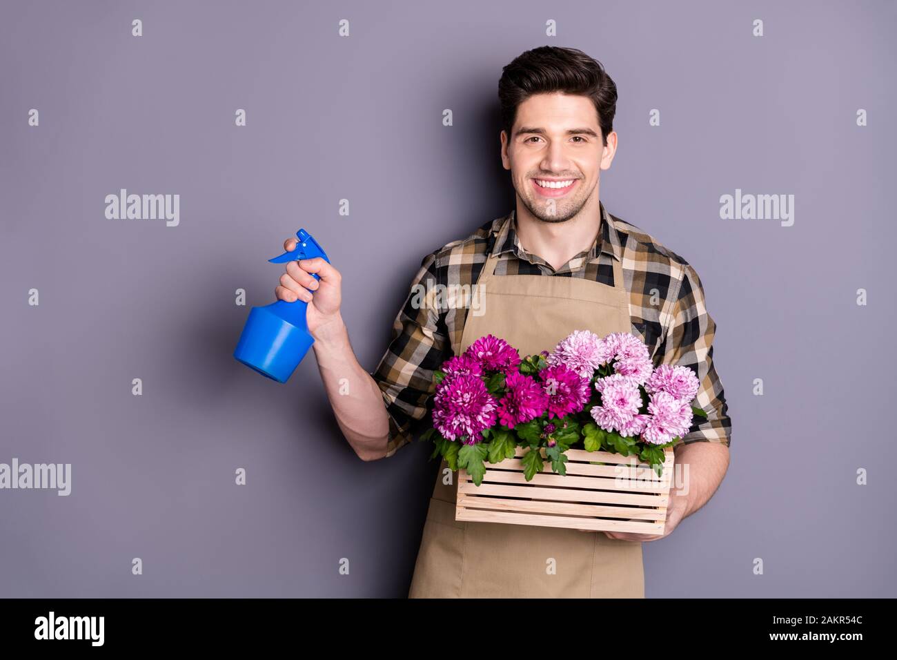 Ritratto di positivo allegro uomo fiorista lavoratore avere proprio piccolo giardino cura di piante fiori spray indossare spray camicia a scacchi plaid isolato Foto Stock