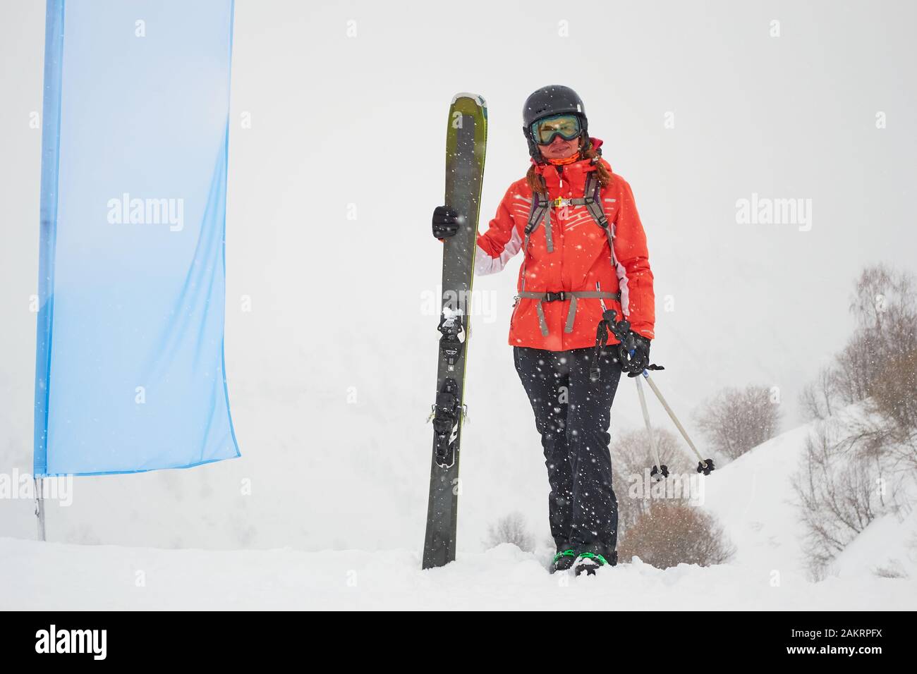 Freerider donna sciatore con grasso / largo tutti gli sci di montagna in posa accanto a una bandiera blu bianco, durante una giornata bianca nella stazione sciistica di Les Sybelles, Francia. Foto Stock