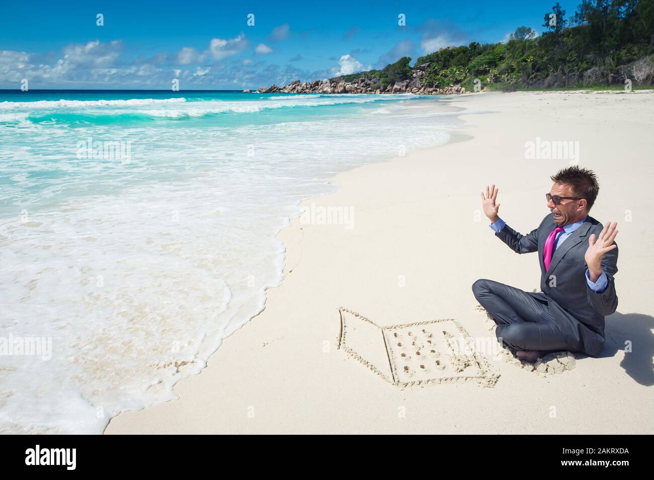 Imprenditore lavorando sul suo computer portatile di sabbia sulla spiaggia sempre interrotto da un onda che sopraggiungono Foto Stock