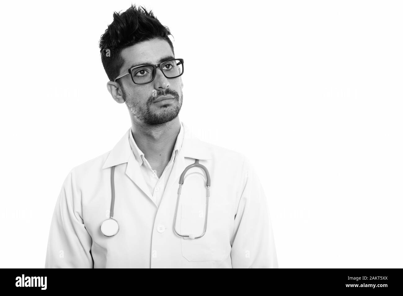 Studio shot del giovane uomo persiano medico pensando indossando occhiali da vista Foto Stock