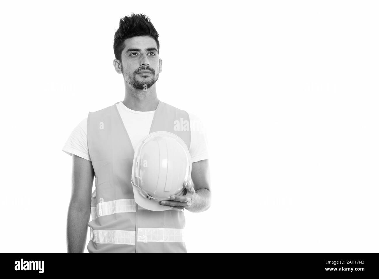 Studio shot del giovane uomo persiano lavoratore edile azienda casco di sicurezza mentre il pensiero Foto Stock