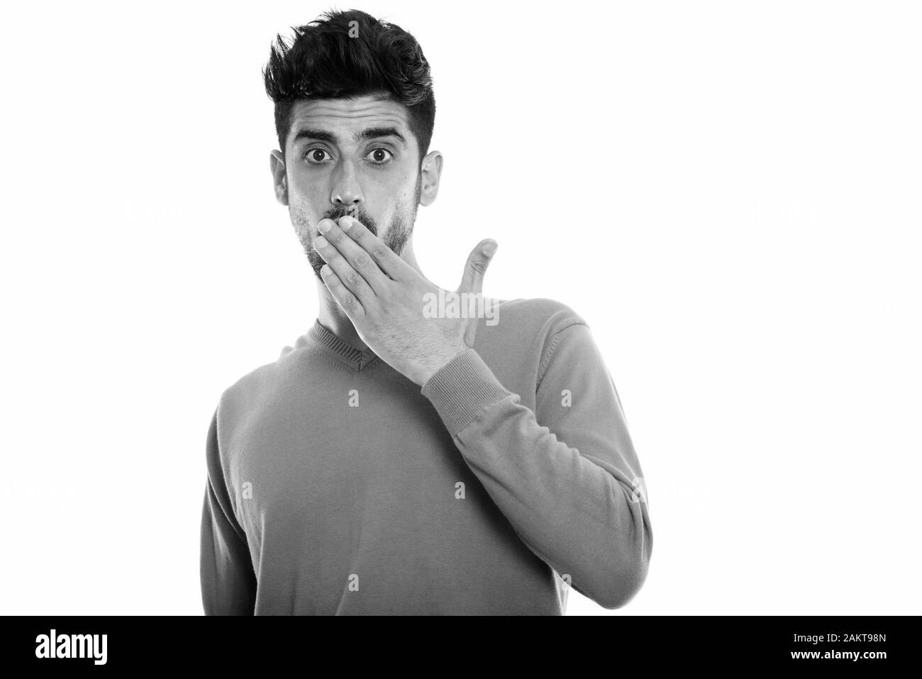 Studio shot del giovane uomo persiano guardando sorpreso mentre copre la bocca Foto Stock