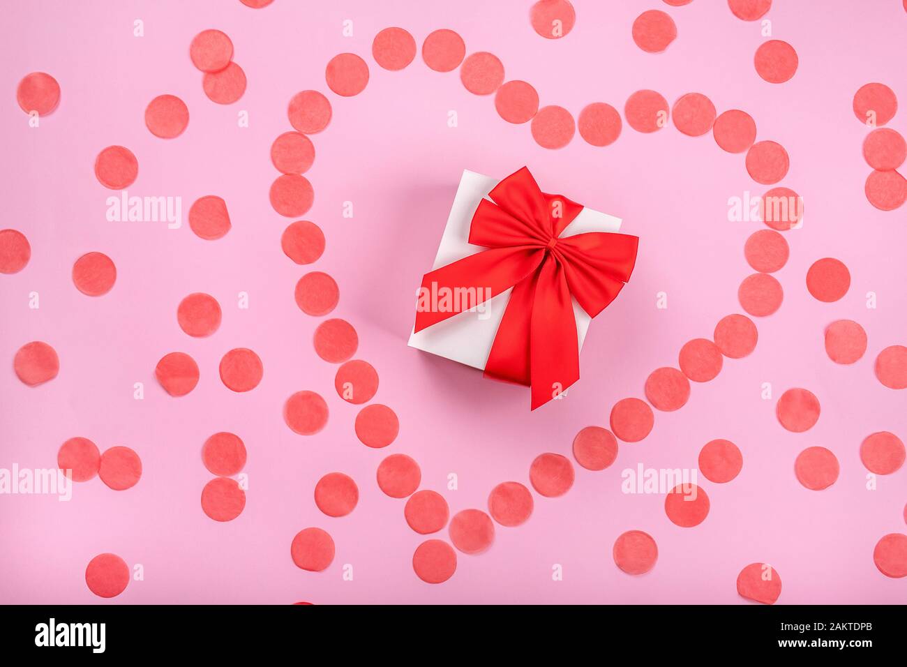 Confezione regalo con fiocco rosso e coriandoli a forma di cuore intorno Foto Stock
