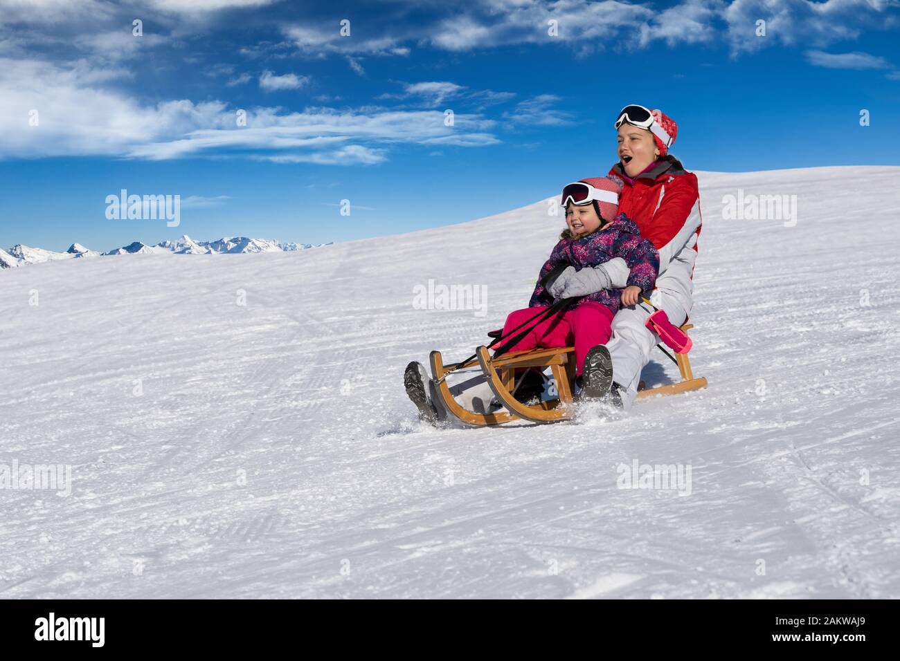 Felice giovane madre e la sua piccola figlia Toddler godendo di un giro in slitta in Winter Park Foto Stock