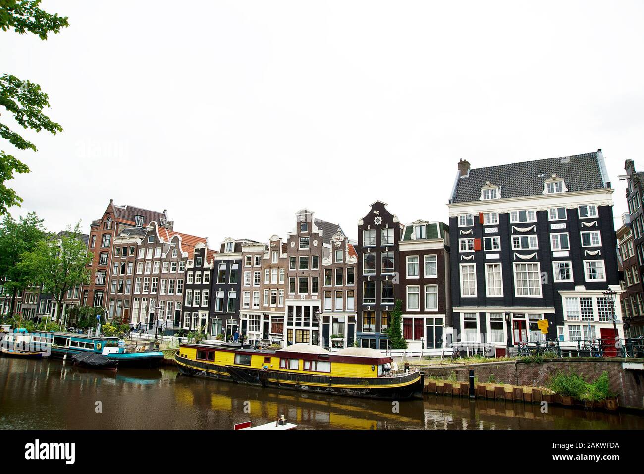 Lato canale di Amsterdam che mostra le tradizionali case sul lato canale con la chiatta gialla ormeggiata sul canale Foto Stock