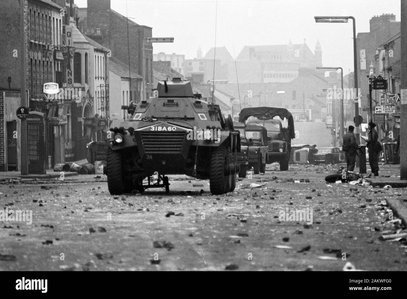 Auto blindate rumble oltre le macerie passato auto rovesciate e distrutto un ciclo motore all'alba in Belfast protestante di Shankill Road, dopo una notte di violenza in cui tre persone sono morte. Foto Stock