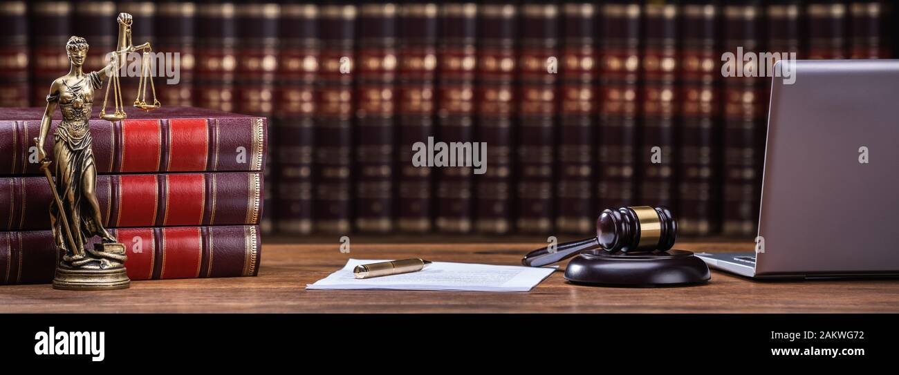 Primo piano di un mazzuolo e libro legale con giustizia scala su tavola in aula Foto Stock