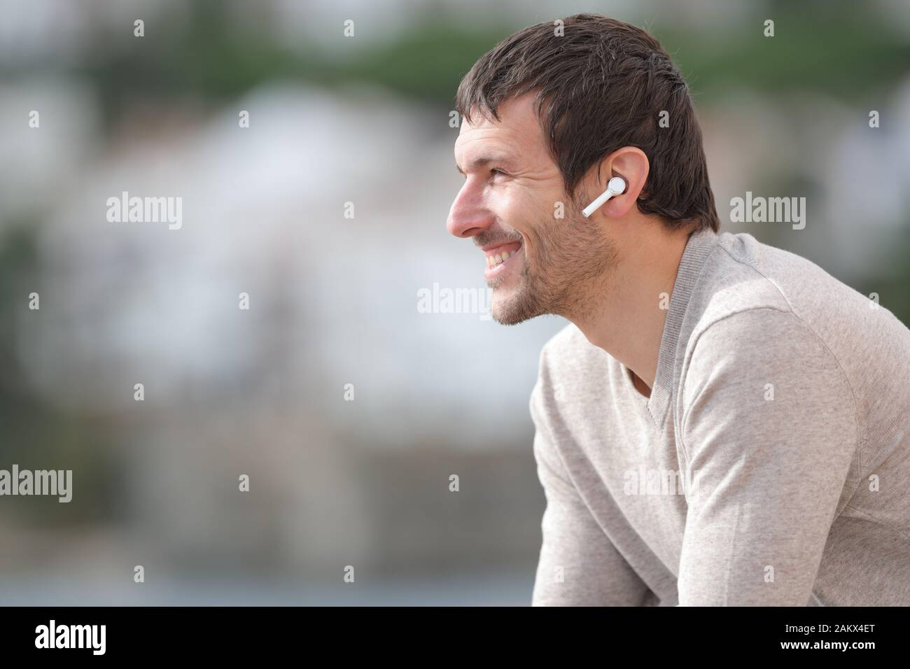 Profilo di un uomo felice l'ascolto di musica con cuffie wireless in una città costiera Foto Stock